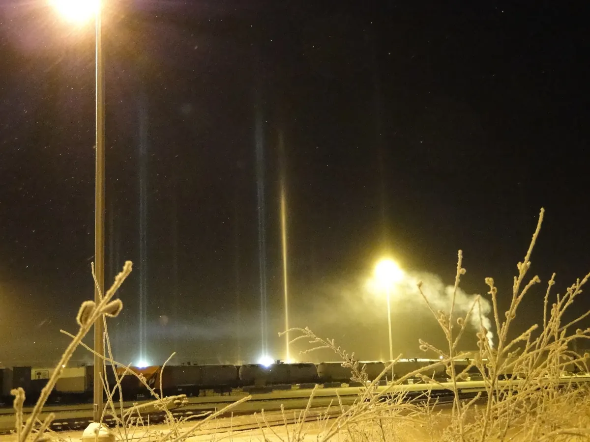 Bright vertical light pillars rising from streetlights through ice fog on a winter night