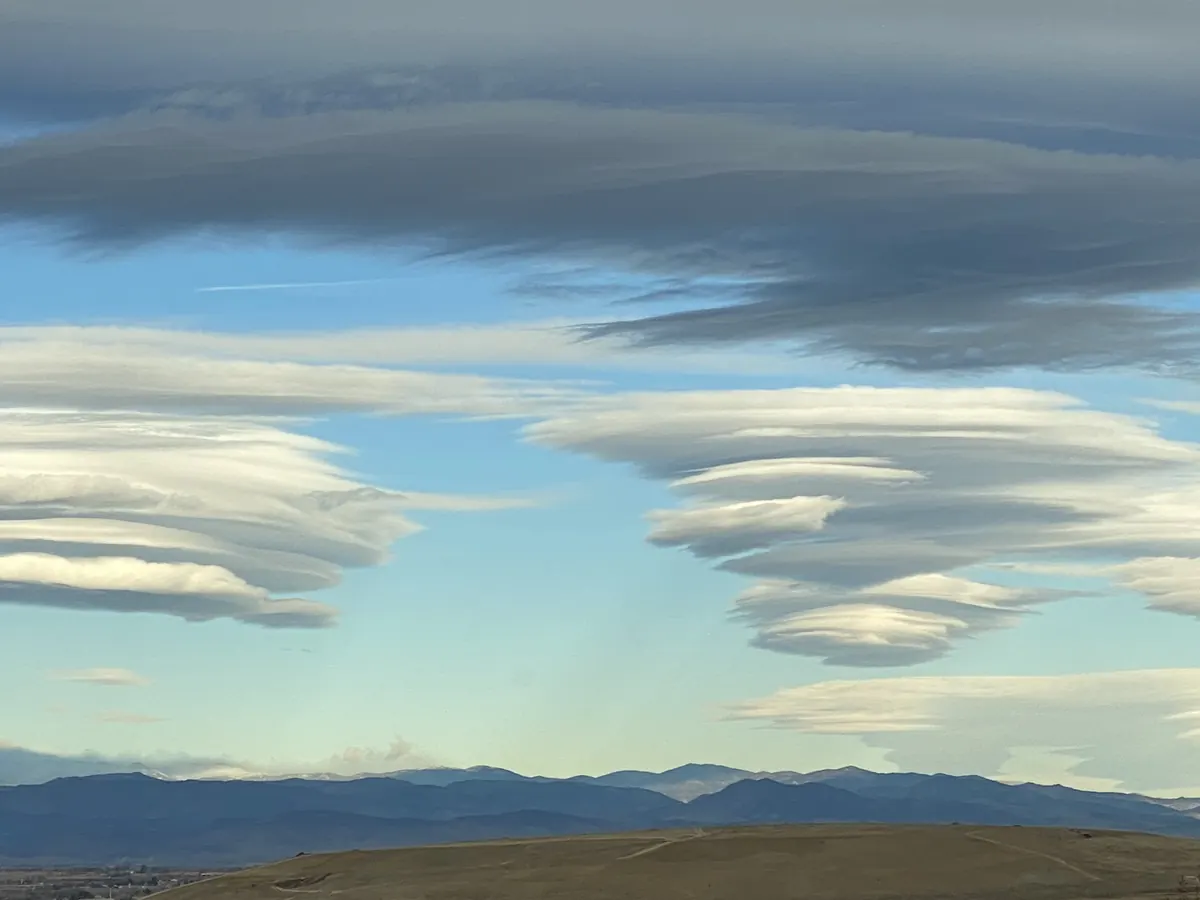 Stacks of smooth, lens-shaped clouds hanging over the dark foothills of the Front Range.