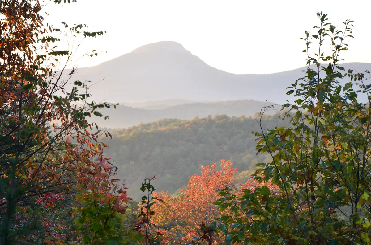 Orange and red maples framing a hazy view of Mount Yonah's rounded summit above forested ridges in early morning light