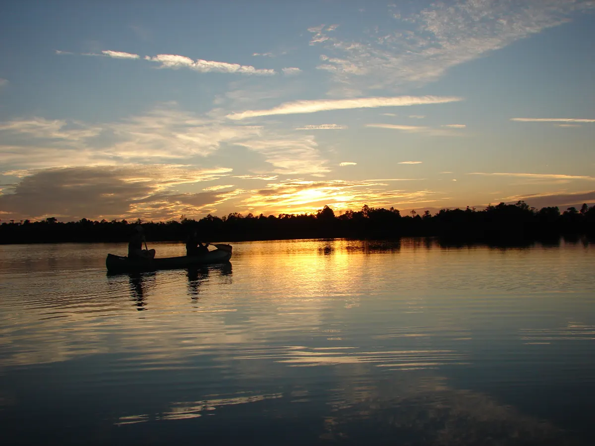 Two canoeists silhouetted on still black water under a sunset sky streaked with thin clouds at Chesser Prairie in the Okefenokee