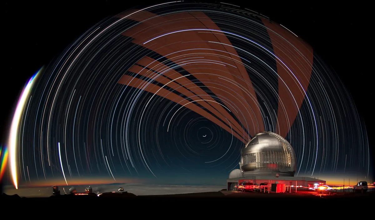 A fish-eye night view on Maunakea: star trails circle the sky above the silver Gemini North telescope dome, a laser beam sweeps overhead, and clouds lie below the summit.