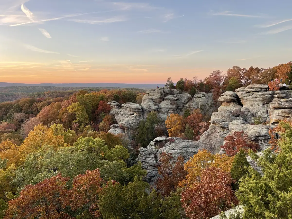 Sandstone rock formations rising above hills of orange, red and yellow autumn trees under an evening sky at Garden of the Gods