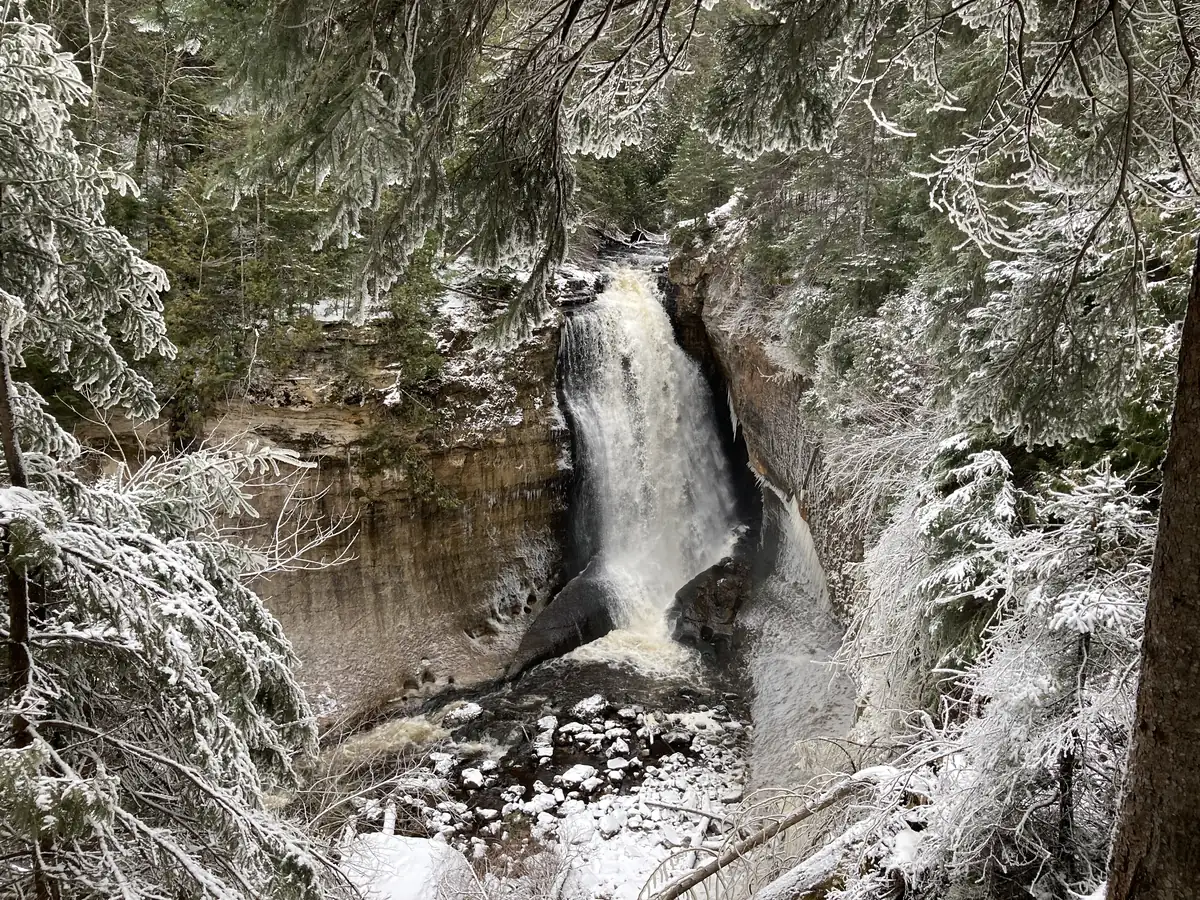 Miners Falls pouring over a sandstone ledge between snow-covered, ice-coated trees
