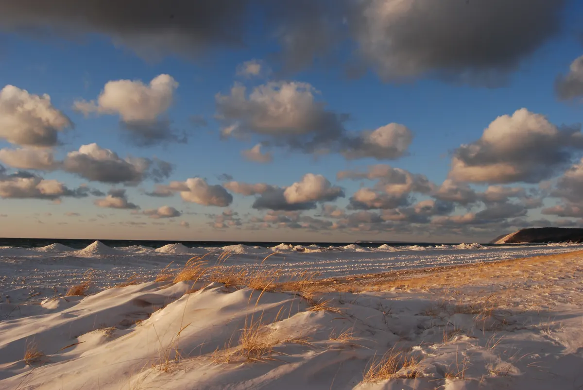 Mounds of shelf ice along a Lake Michigan beach with snow-dusted dune grass in front