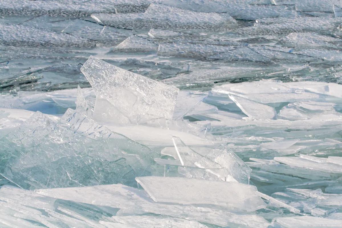 Clear plates of lake ice stacked and tilted on top of each other after being pushed together