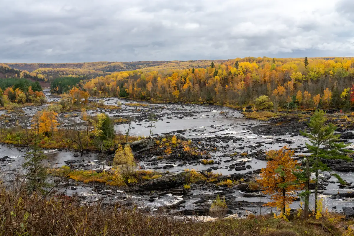The St. Louis River flowing over dark rock between banks of yellow, orange and green trees.
