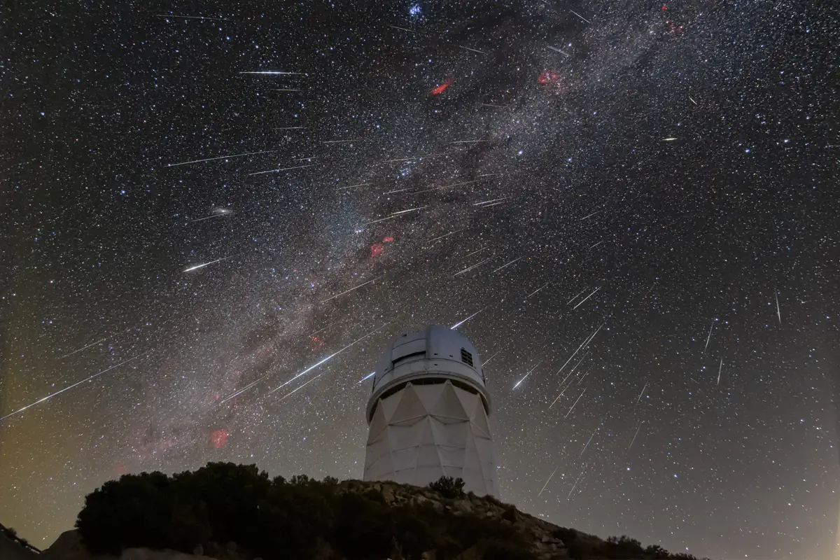Dozens of meteor streaks and the Milky Way across a starry sky above a white telescope dome on a dark hilltop