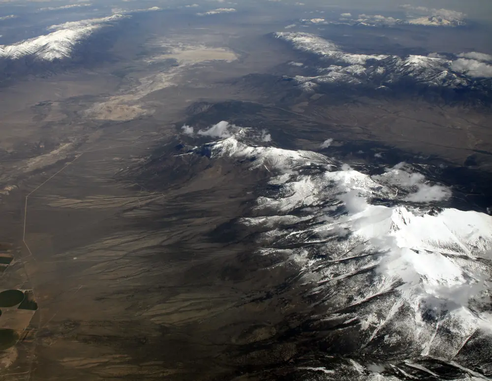 Aerial view of the snow-covered Snake Range and Wheeler Peak above a dry valley floor.