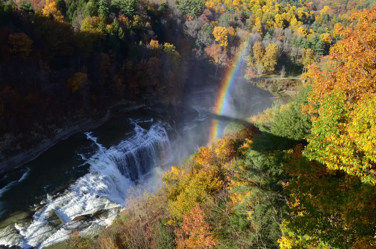The Upper Falls of the Genesee River at Letchworth State Park, seen from above among trees in autumn color, with a rainbow in the spray.
