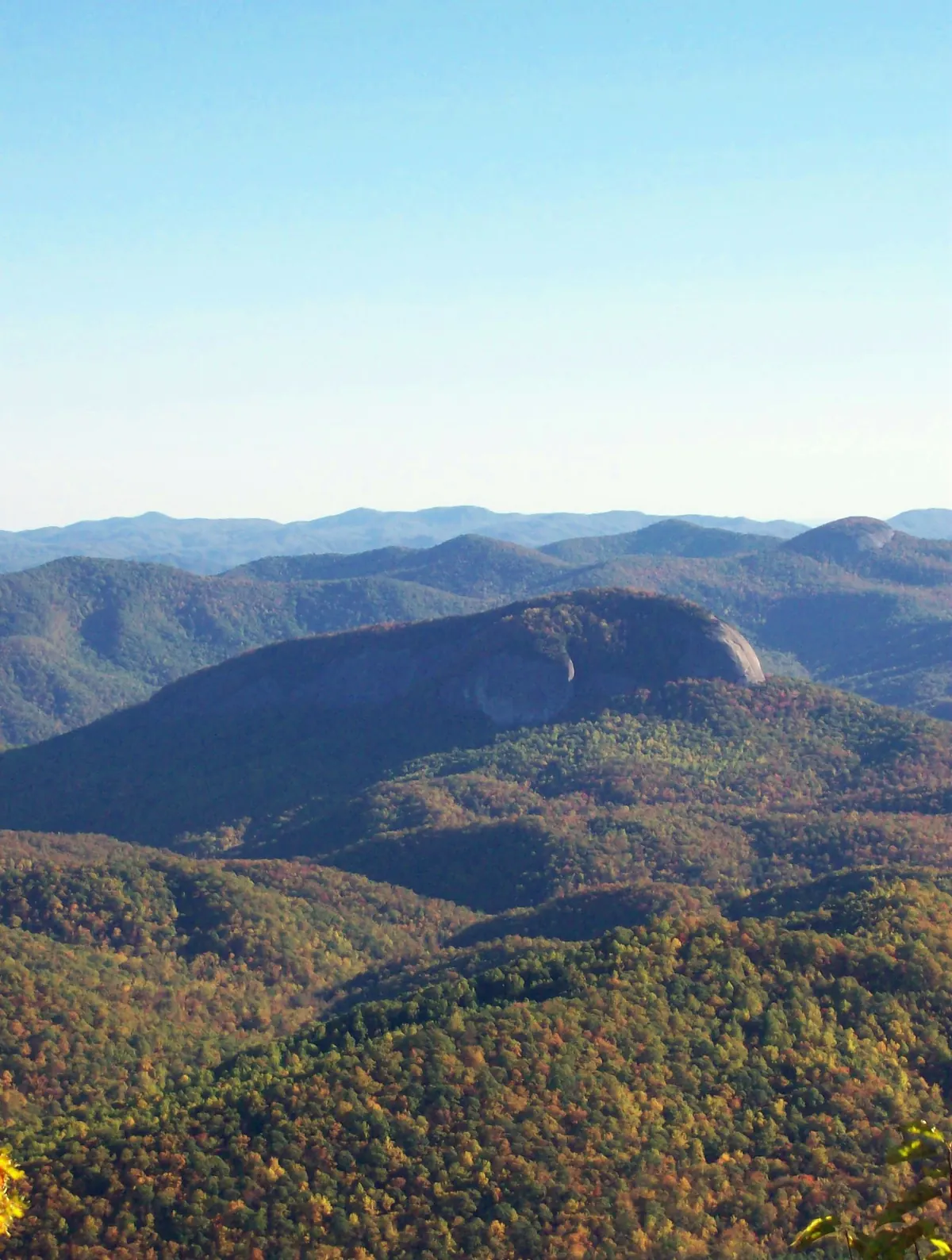 The bare granite dome of Looking Glass Rock rising above forested ridges of Pisgah National Forest that are beginning to turn autumn colors