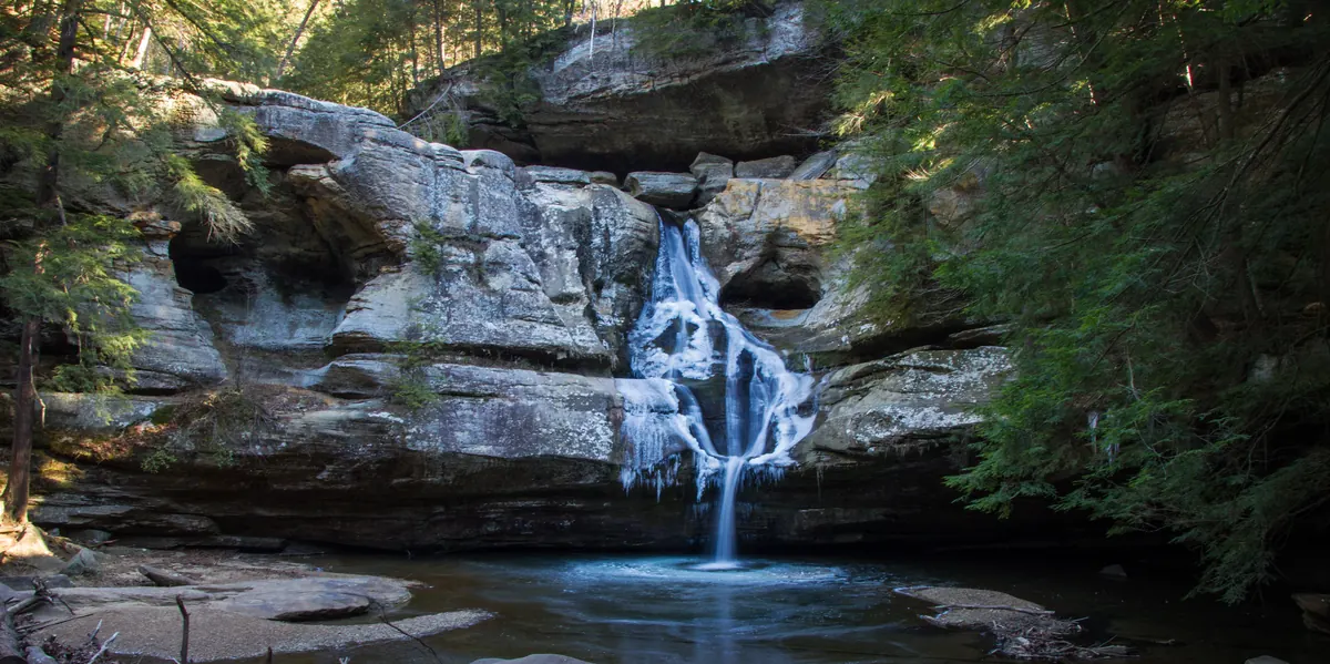 Cedar Falls in the Hocking Hills, a waterfall over gray sandstone ledges edged with ice and framed by dark hemlocks.