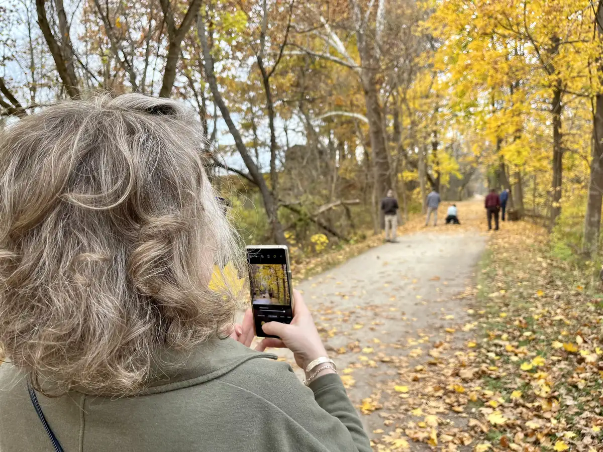 A visitor photographs the Ohio and Erie Canal Towpath in Cuyahoga Valley National Park, the trail lined with yellow and orange autumn trees.