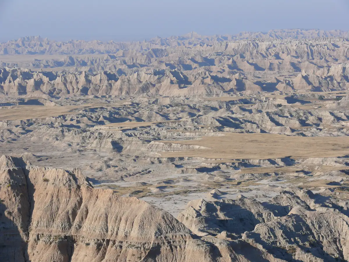 Early sun lights the pale, eroded buttes and spires of Badlands National Park above a grassy basin.