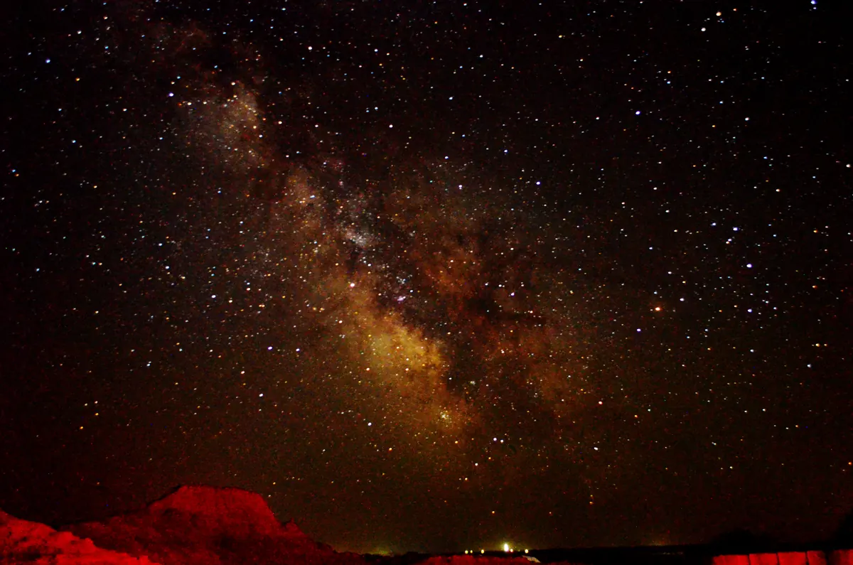 The Milky Way arches over a dark horizon under a star-filled night sky.