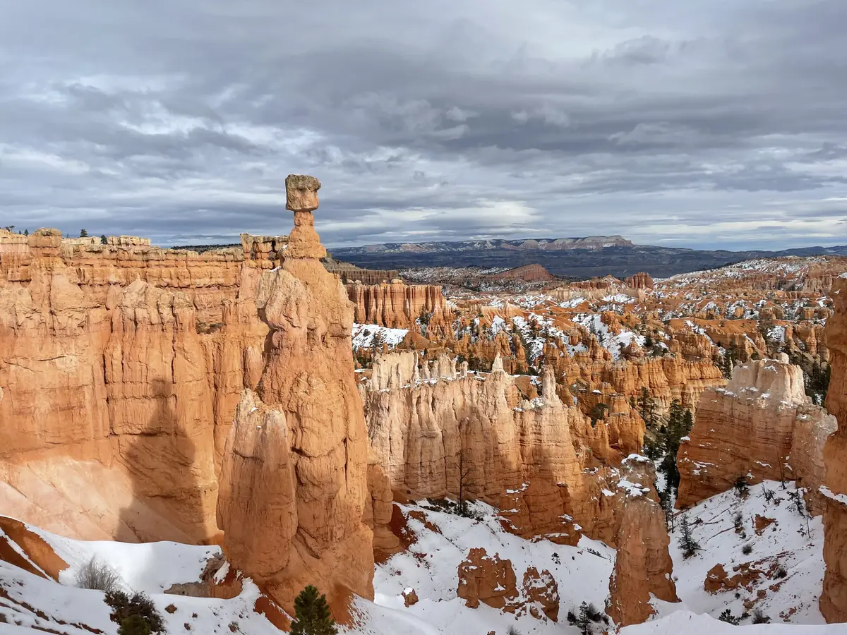 Orange hoodoos and cliffs at Bryce Canyon dusted with snow under a gray sky