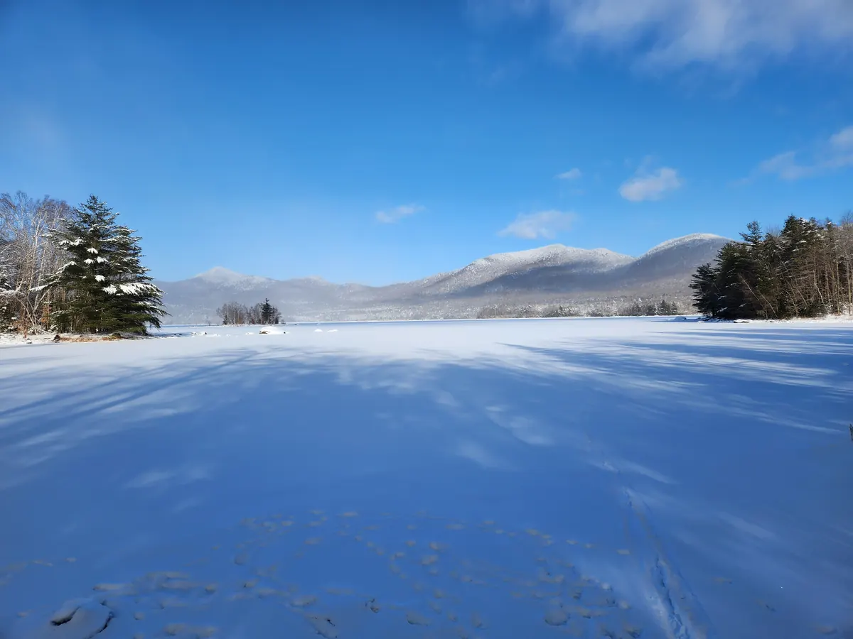 A snow-covered reservoir with snow-laden trees along the shore and white mountains in the distance.