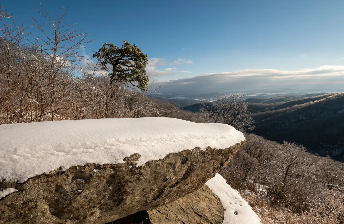 A snow-covered boulder on a Blue Ridge overlook in Shenandoah National Park, with ice-coated bare trees and snowy valleys stretching to the horizon