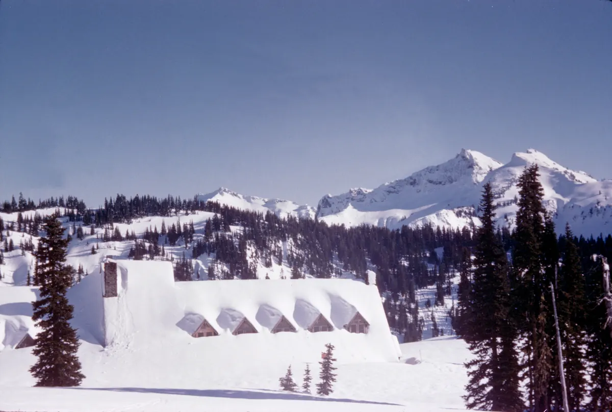 Paradise Inn on Mount Rainier half buried under deep snow, with snowy slopes rising behind it.
