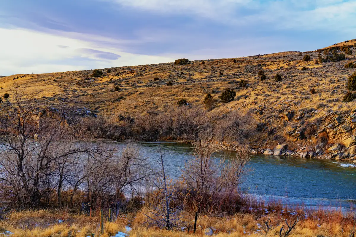The North Platte River curving below a dry, grassy hillside dotted with rocks and bare shrubs